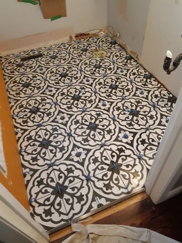Black and white patterned tiles being installed on a bathroom floor.