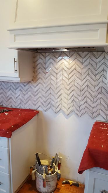 Kitchen backsplash installation with chevron tiles in progress.