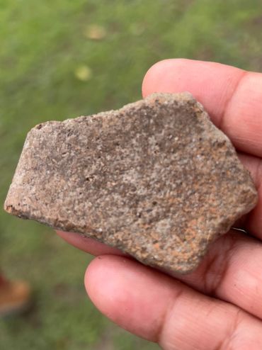 Hand holding a small, rough, brownish rock outdoors.
