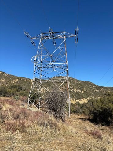 Power transmission tower on a dry hillside under a clear blue sky.