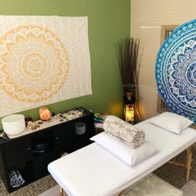 Massage table with soft blankets and pillows. Low lighting and singing bowls in the background.