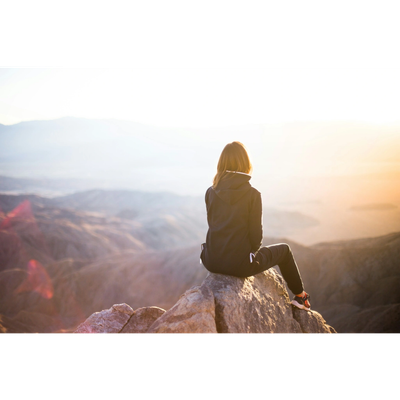 Person sitting on a rock overlooking a vast mountainous landscape at sunrise.