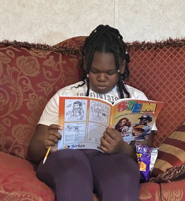 A Young Black Girl on a couch going through our puzzles in the activity book