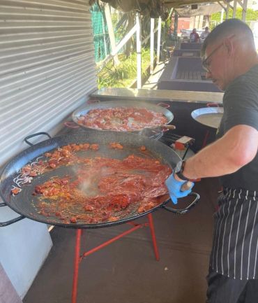 Man cooking large pans of food outdoors.