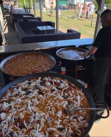 Large pans of seafood paella being cooked outdoors.