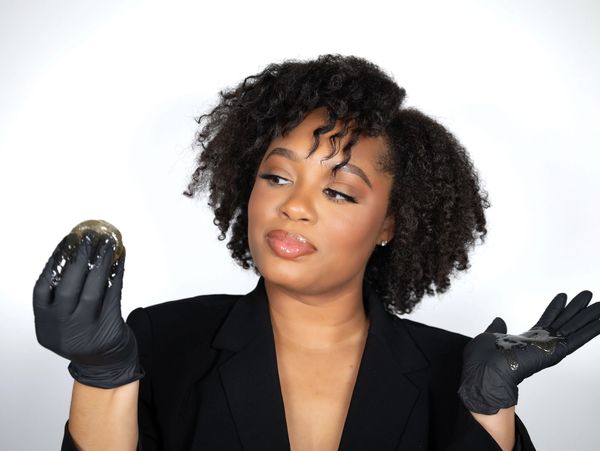 Woman wearing black gloves holds and examines a shiny, slimy substance with curiosity.