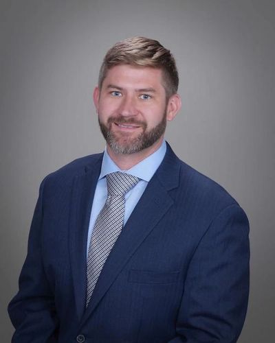 Professional man in a navy suit with a light blue shirt and patterned tie.