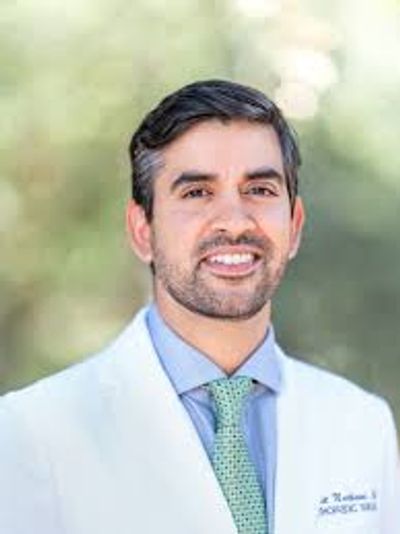 A smiling doctor in a white coat outdoors.