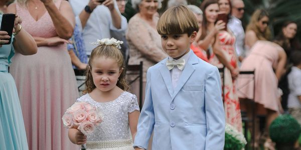 A young flower girl holding a small bouqet and ring bearer in a blue suit walk down the aisle.