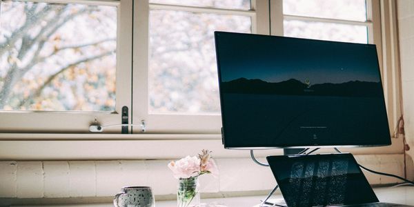 We see a computer on a desk with a view out a window to trees, it looks like autumn.