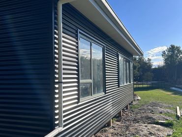Side view of a modern house with black corrugated metal siding and a white gutter pipe.
