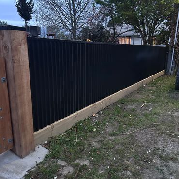 A modern black metal fence with wooden posts and base in a garden.