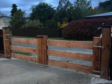 A sturdy wooden gate with metal hinges stands at a driveway entrance.