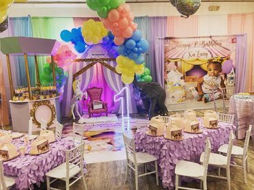 Colorful carnival-themed first birthday party with balloons, decorations, and a big photo of the birthday child.