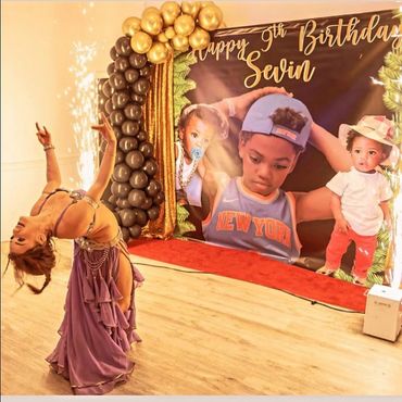 A dancer performs in front of a birthday backdrop with balloons and sparklers.