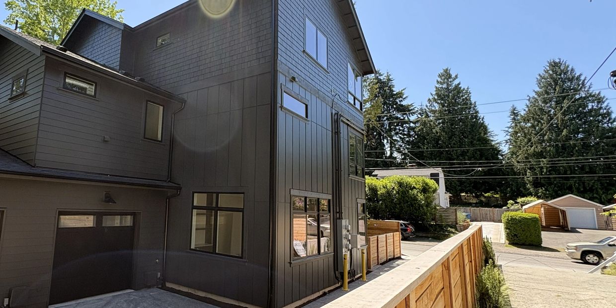 Modern dark gray house under clear blue sky with wooden fence.