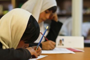 Two South Asian girls write at a shared table.