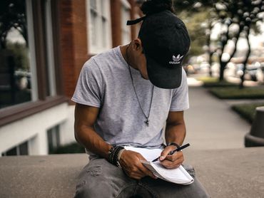 Young man outside a building writes in notebook on concrete bench.
