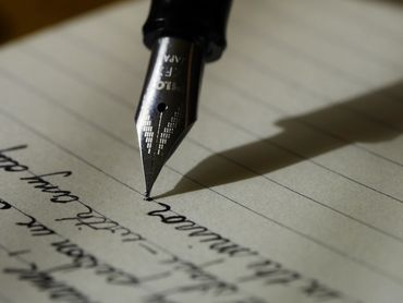 Closeup of a fountain pen poised to complete a sentence on lined paper.