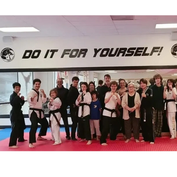 a group of taekwondo students and their parents pose for a photo on the mat