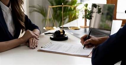 Two people discussing legal documents at a desk with scales of justice.