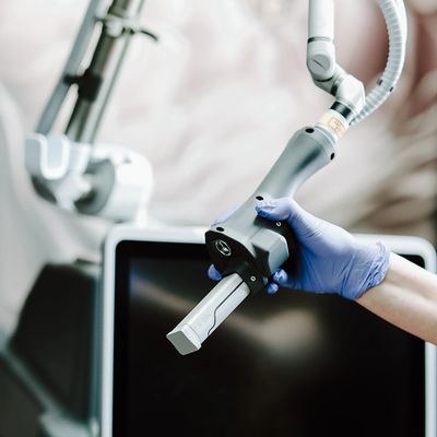 Hand holding a medical laser device with a screen in the background.
