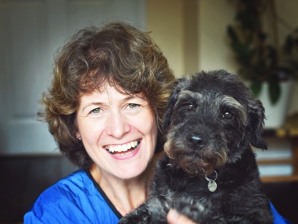 Smiling woman holding a fluffy black dog indoors.