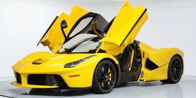 Yellow Ferrari sports car with butterfly doors open in a studio setting.