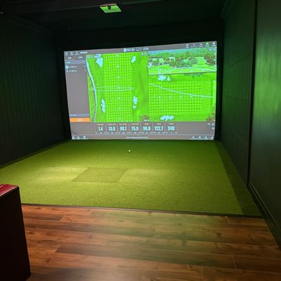 Indoor golf simulator room with a green turf and projected golf data.
