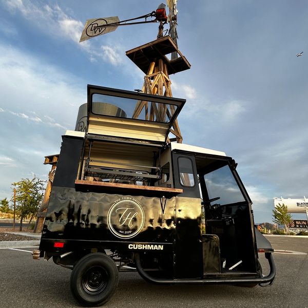 A black Cushman food truck with open service window under a wooden windmill.