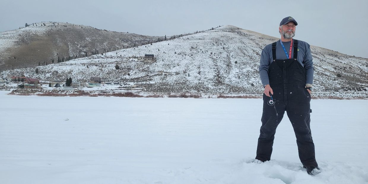 Man in winter clothing standing on a snowy landscape holding a fishing rod.