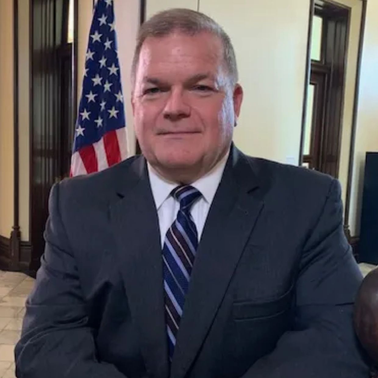 Man in a suit with an American flag in the background.