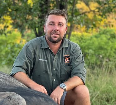 Man in green shirt posing with a large buffalo in a natural setting.
