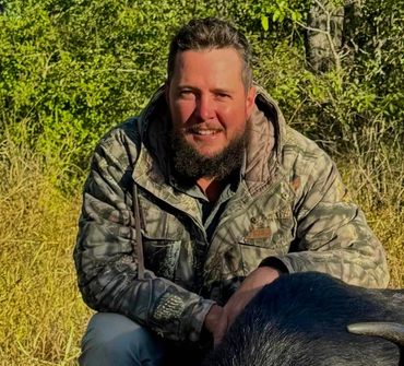Man posing with a large buffalo in a forest clearing.