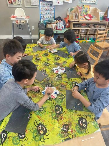 Children painting on black paper at a colorful table in a classroom.