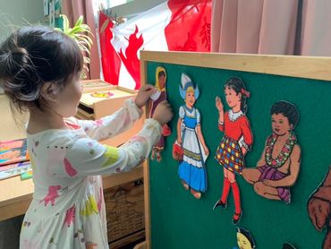 A young girl arranging cultural paper dolls on a felt board in a classroom.