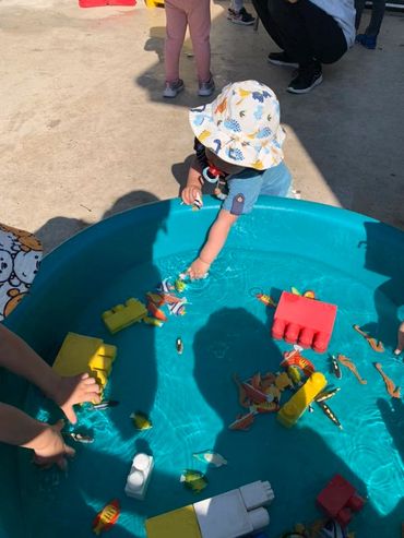 A child plays with water and toy fish in a blue plastic pool.