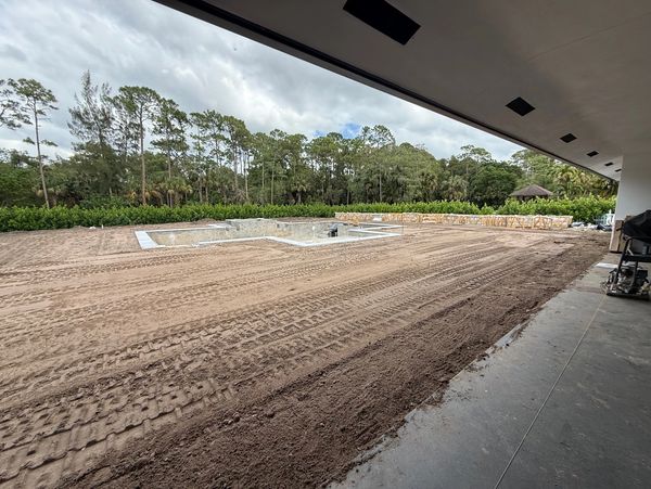 A backyard under construction with a pool excavation and fresh soil.