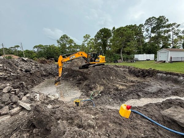 Yellow excavator digging a large muddy hole at a construction site.