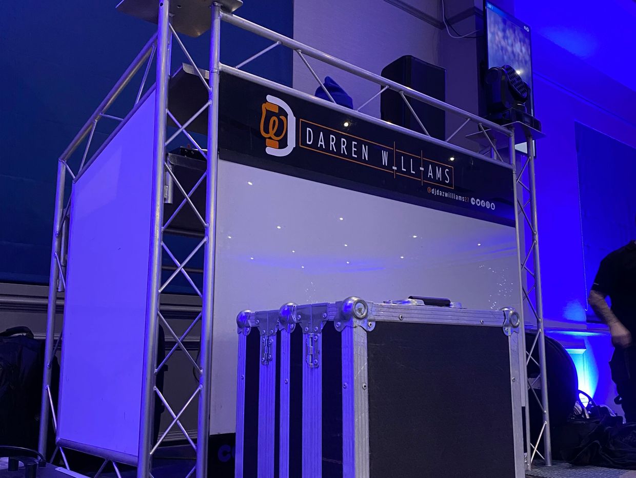 DJ booth setup with lighting and equipment in a blue-lit room.