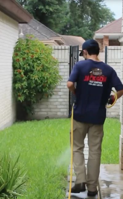 Pest control technician applying treatment along the exterior wall of a residential home.