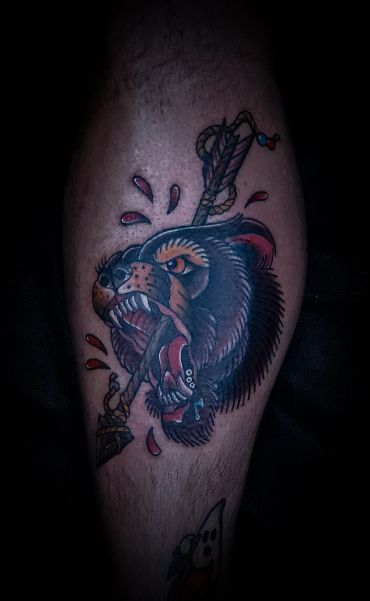 Tattoo of a fierce bear's head pierced by an arrow with blood drops.