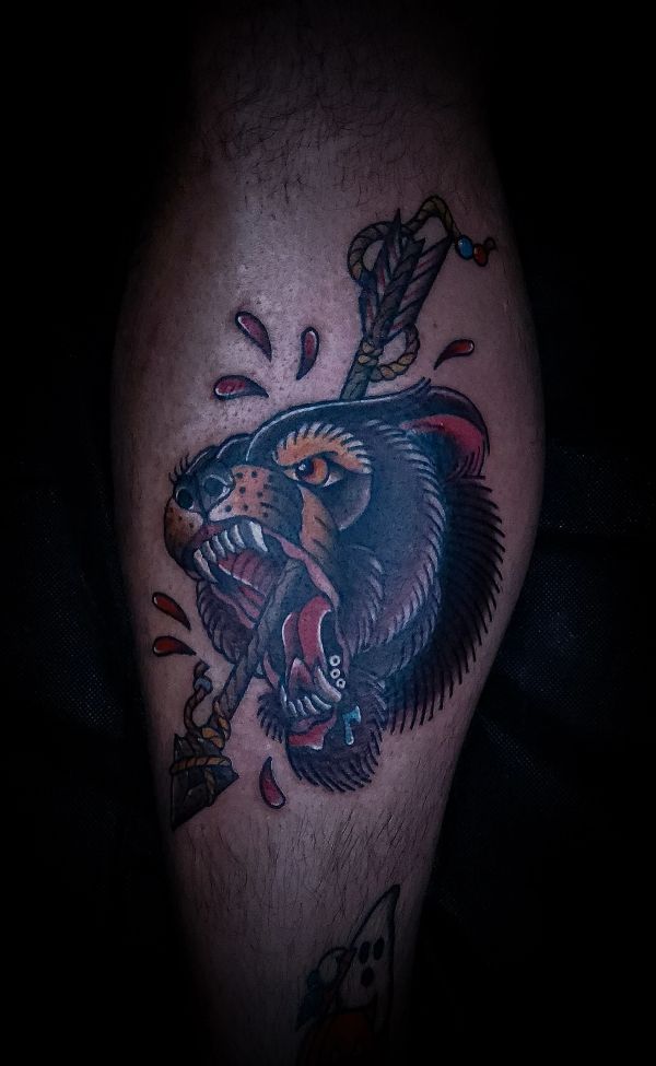 Tattoo of a fierce bear's head pierced by an arrow with blood drops.
