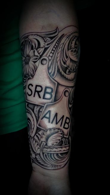 Intricate black and gray tattoo with floral patterns and tags labeled SRB and AMB.