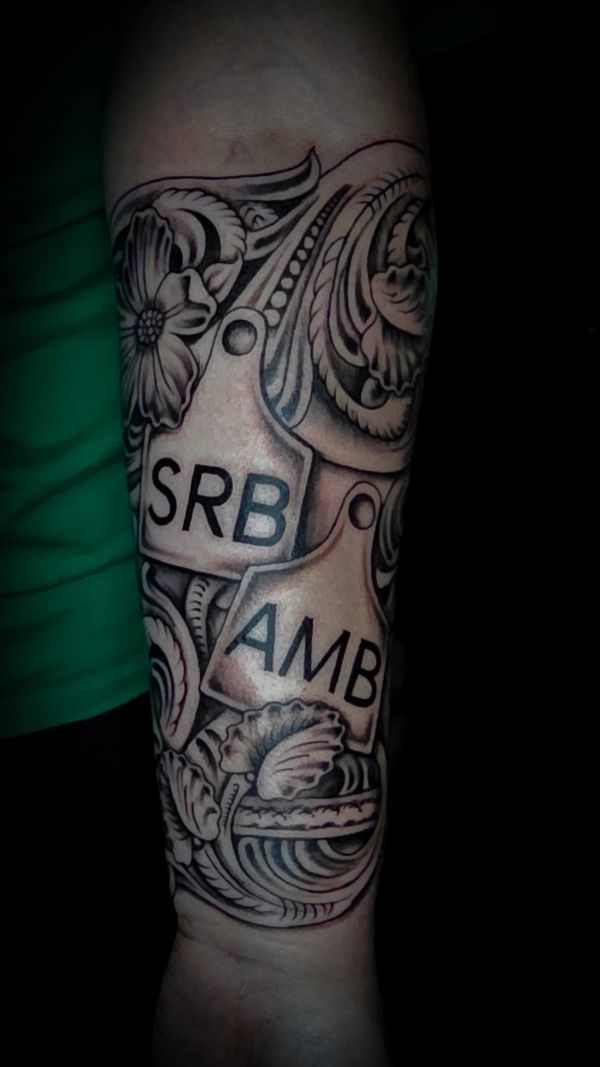 Intricate black and gray tattoo with floral patterns and tags labeled SRB and AMB.