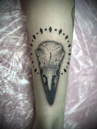Black and gray tattoo of a bird skull with geometric shapes around it.