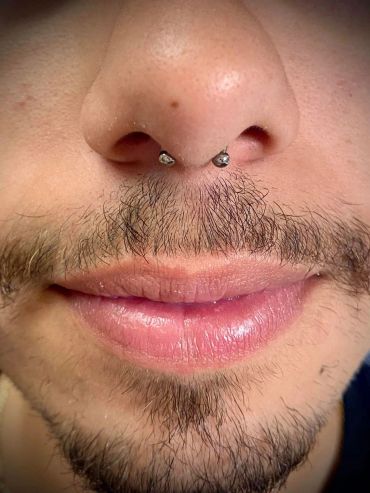 Close-up of a person's lips, mustache, and nose with a septum piercing.