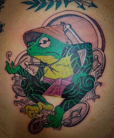 Colorful tattoo of a meditative frog wearing a hat and scarf with intricate patterns.