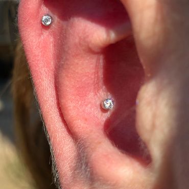 Close-up of an ear with two shiny stud piercings on the inner part.