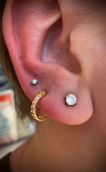 A close-up of an ear with three different stud and hoop earrings.